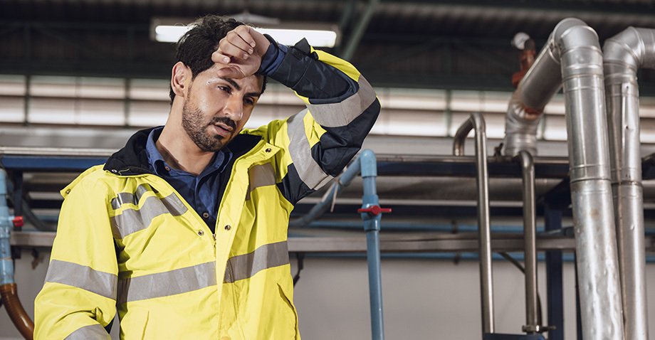 Lavoratore in cantiere o ambiente industriale si asciuga la fronte per il caldo, immagine sul rischio di colpo di calore sul lavoro